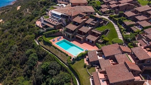 An aerial view of a coastal residential area with terracotta-roofed houses, a central swimming pool, and lush greenery. - SAN TEODORO PUNTA EST TRILOCALE MERAVIGLIOSA VISTA MARE (Capo Coda Cavallo)