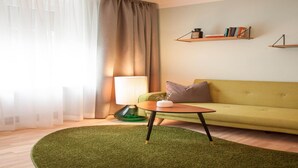 Una sala de estar con un sofá verde, una mesa de centro redonda, una lámpara y una alfombra verde.