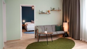 Sala de estar con sofá, una mesa redonda y una lámpara. Hay dos estanterías en la pared con plantas y libros.