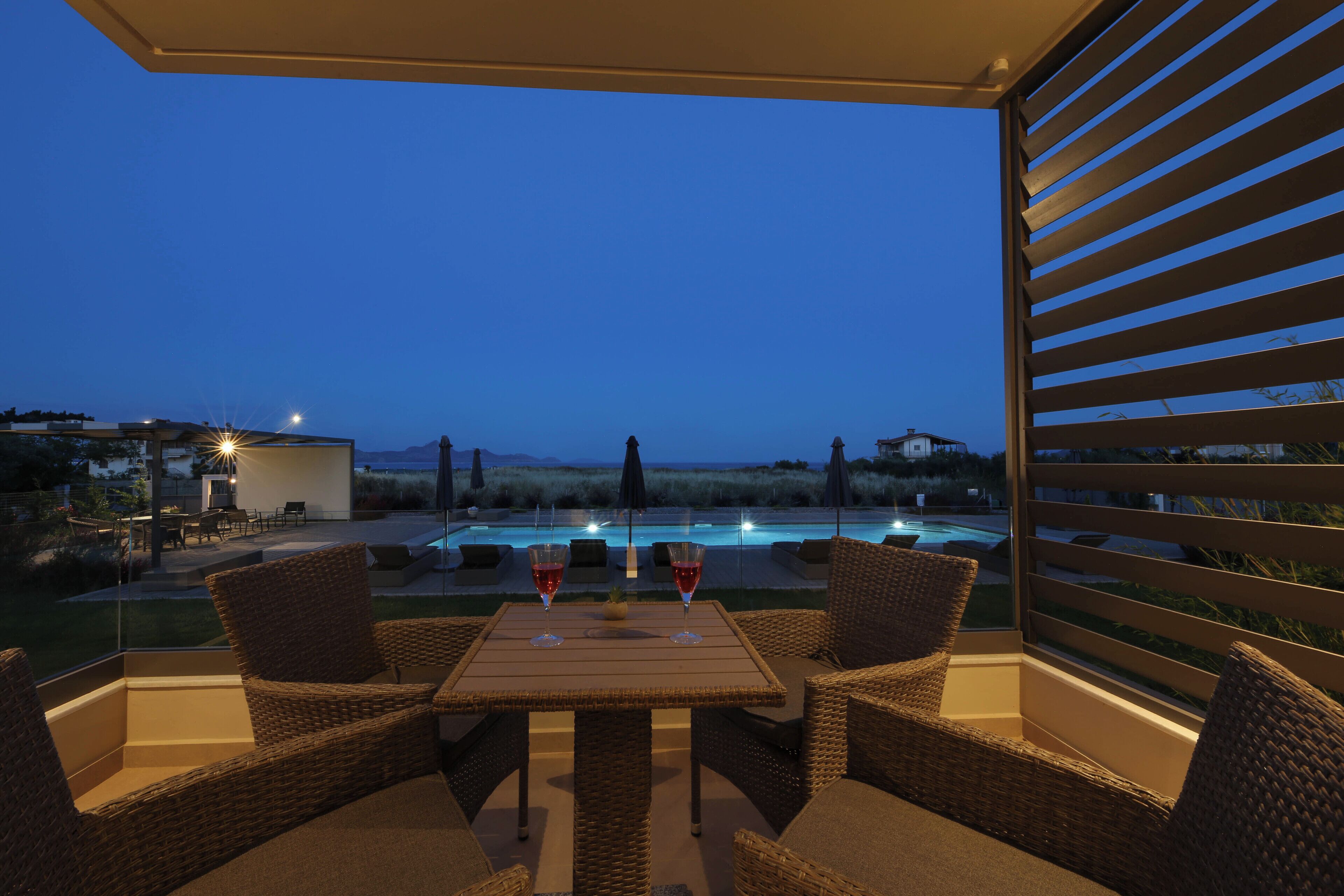Un patio al aire libre con mobiliario de mimbre y una mesa, con vista a una piscina y jardines.