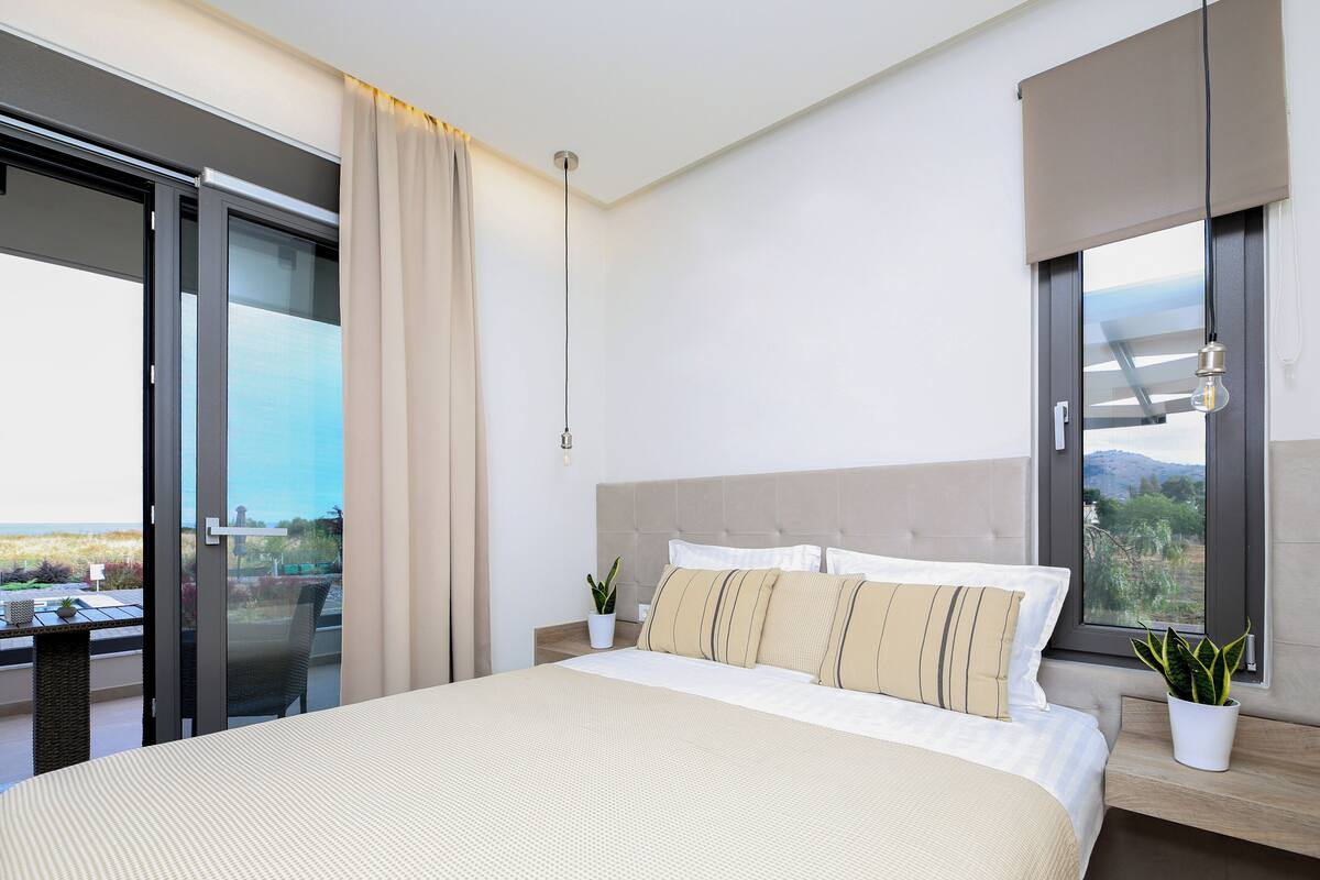 Un dormitorio moderno con una cama grande, un ventanal corredero a un balcón, una planta en maceta y vistas al exterior.