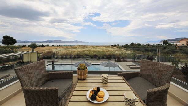 A terrace with wicker furniture, a pool, and a view of the landscape. - Almyres Luxurious Residences  (Argos-Mykines)