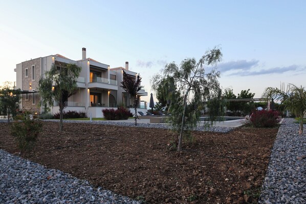 Una casa moderna de dos pisos con jardín ajardinado, que incluye un sendero de piedras y árboles jóvenes.