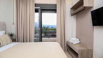 A hotel room with a bed, a TV mounted on the wall, a balcony with curtains, and a view of the outdoors.