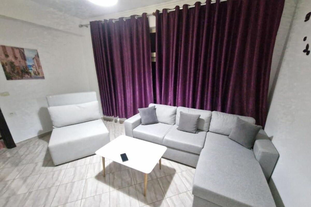 A living room with a white sofa, a white coffee table, and a grey sofa with cushions.