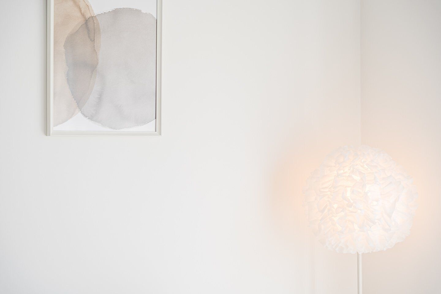 A minimalist room with a framed abstract painting and a textured floor lamp.