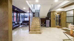 A modern lobby with a staircase, seating area, and a reception desk. - Monday Hotels - Swarna's The Capital (Penumuluru)