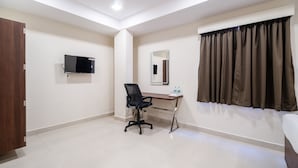 Een hotelkamer met een bureau, stoel, televisie, spiegel en raam met gordijnen.