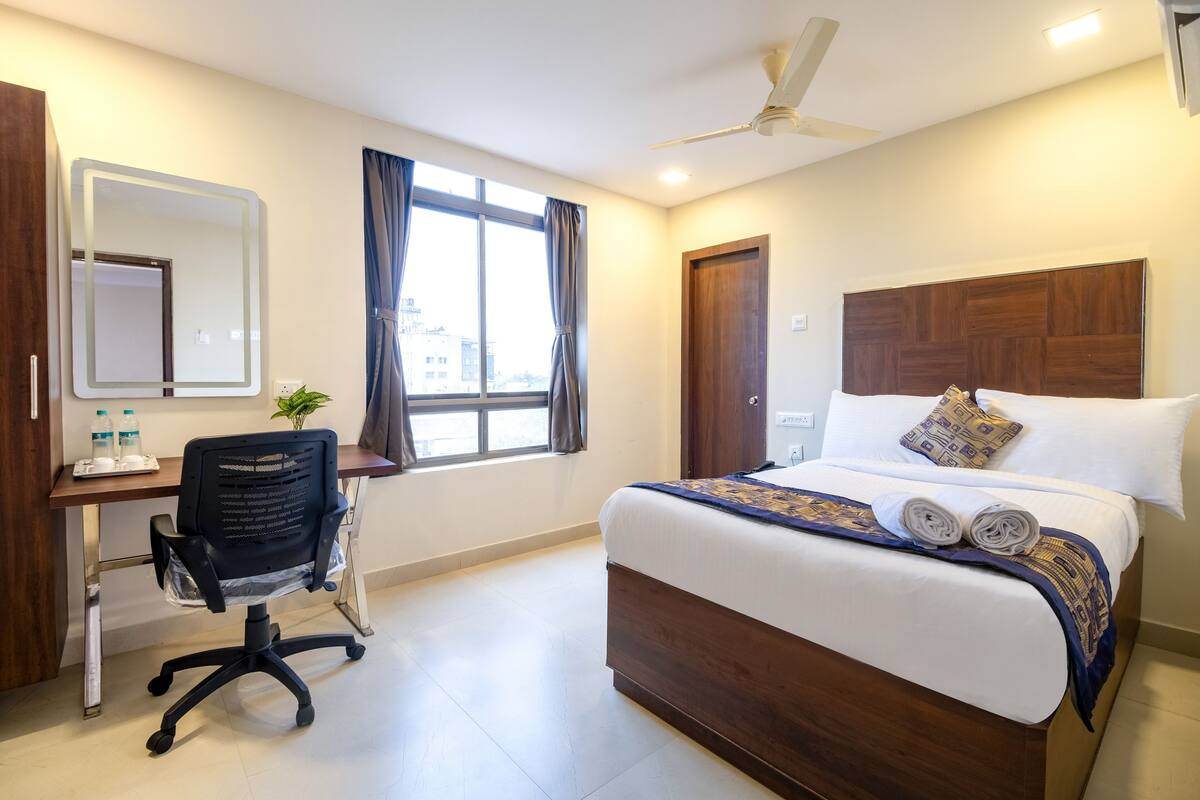 Een hotelkamer met een bed, een bureau met stoel, een grote spiegel en een raam met gordijnen.