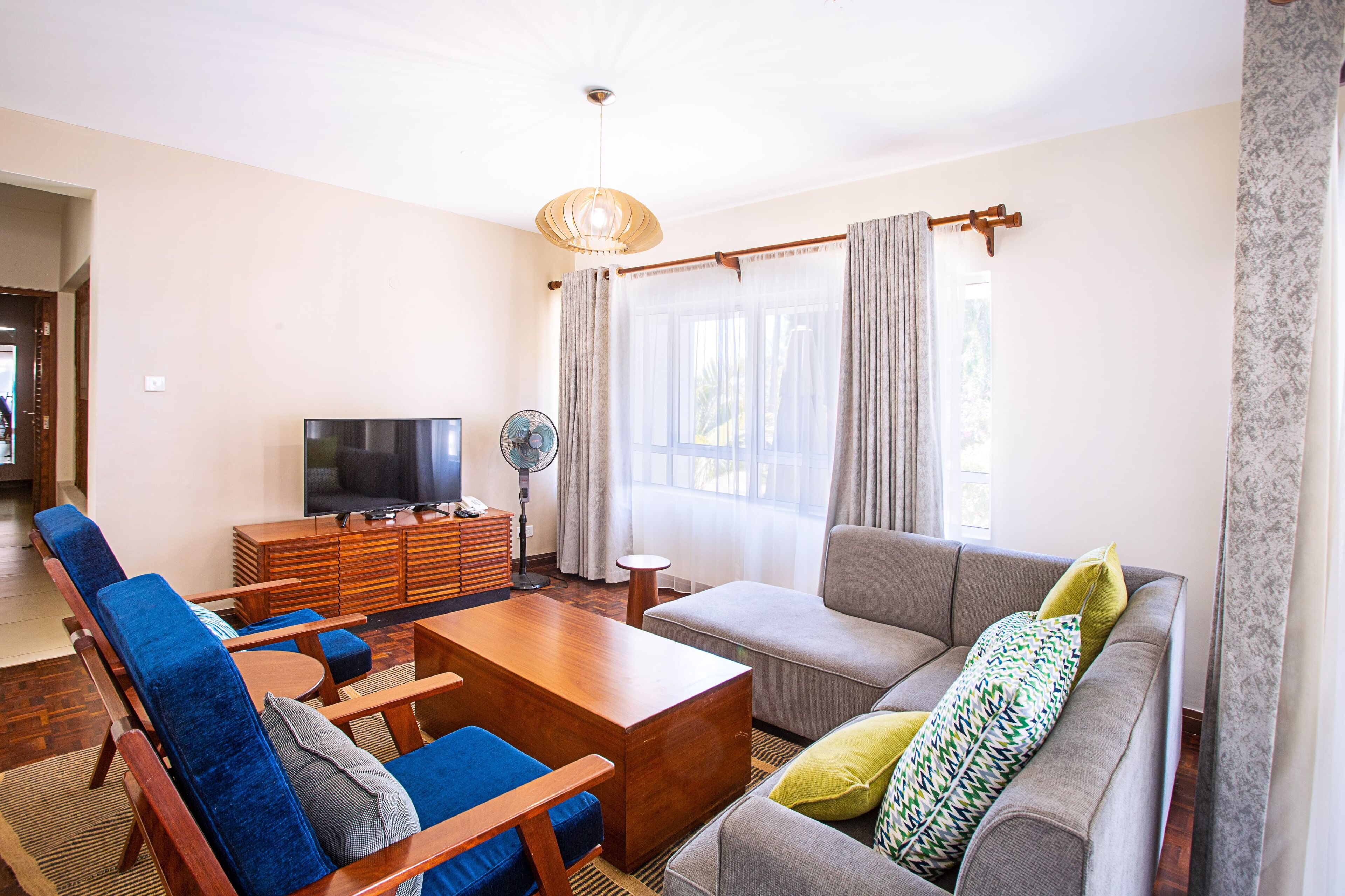 A living room with a sofa, armchairs, a coffee table, a TV, and a fan.