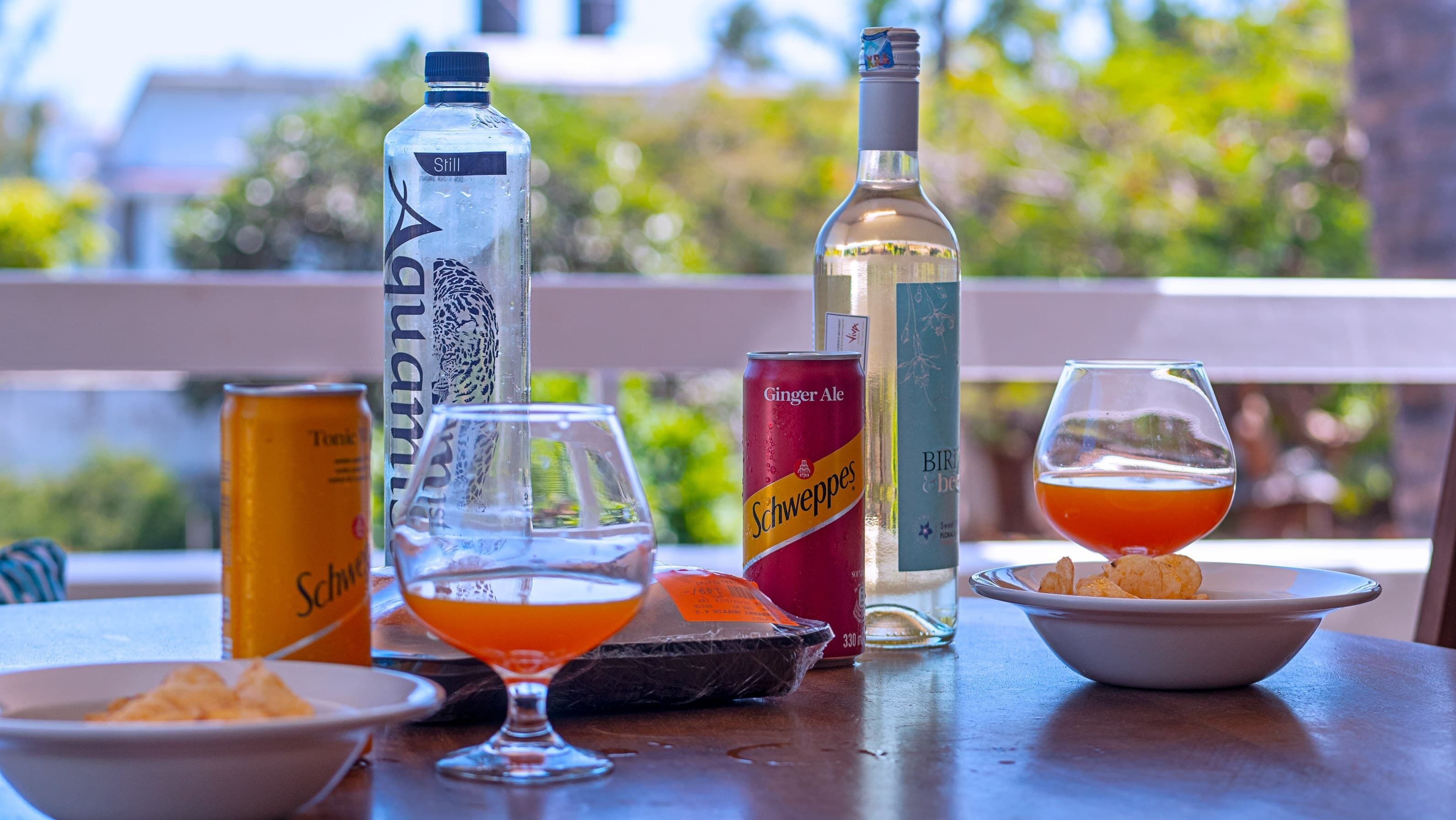 A table with a bottle of Still, a can of Ginger Ale, a glass of orange drink, and a glass of red drink.