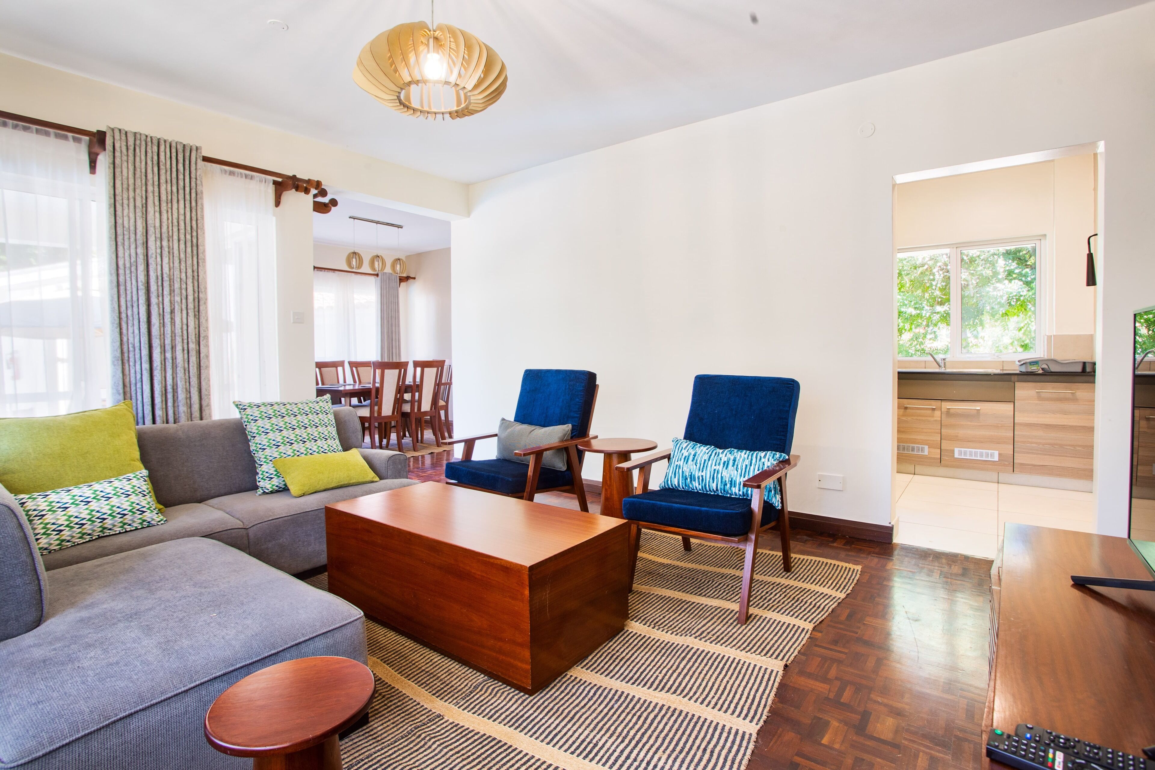 A modern living room with a sofa, armchairs, a coffee table, and a dining area in the background.
