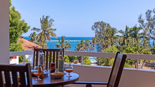 Ein Balkon mit Tisch für zwei Personen, Blick auf einen Strand mit Palmen und das Meer.
