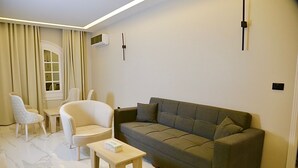 Un salón moderno con un sofá gris, sillones blancos, una pequeña mesa de madera y una ventana con cortinas.