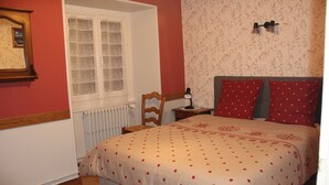 A bedroom with a bed, a chair, a nightstand, a window, and a radiator.