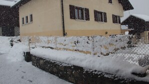 A two-story building with a snow-covered roof and a stone wall in the foreground.