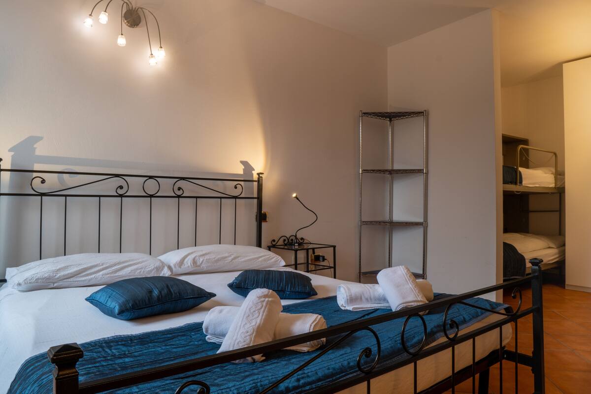 Een net opgemaakt bed met blauw-witte beddengoed, een metalen hoofdbord en een nachtkastje met een lamp.