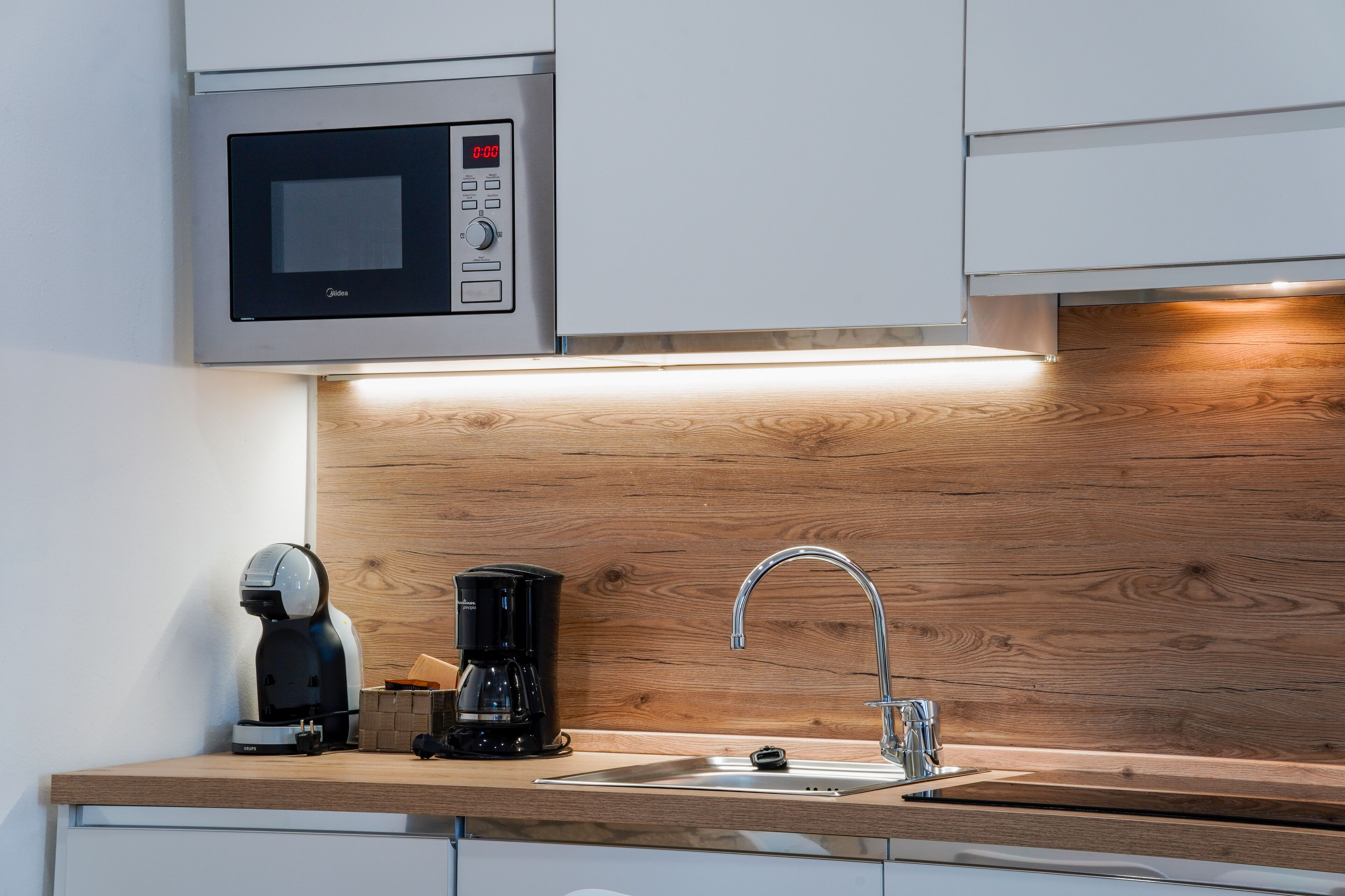 Una cocina moderna con microondas integrado, cafetera y lavamanos.