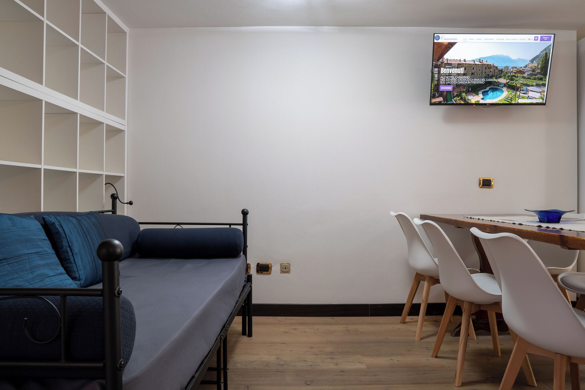 Une pièce comprenant un lit, un téléviseur fixé au mur, une table à manger avec des chaises et un mur blanc.