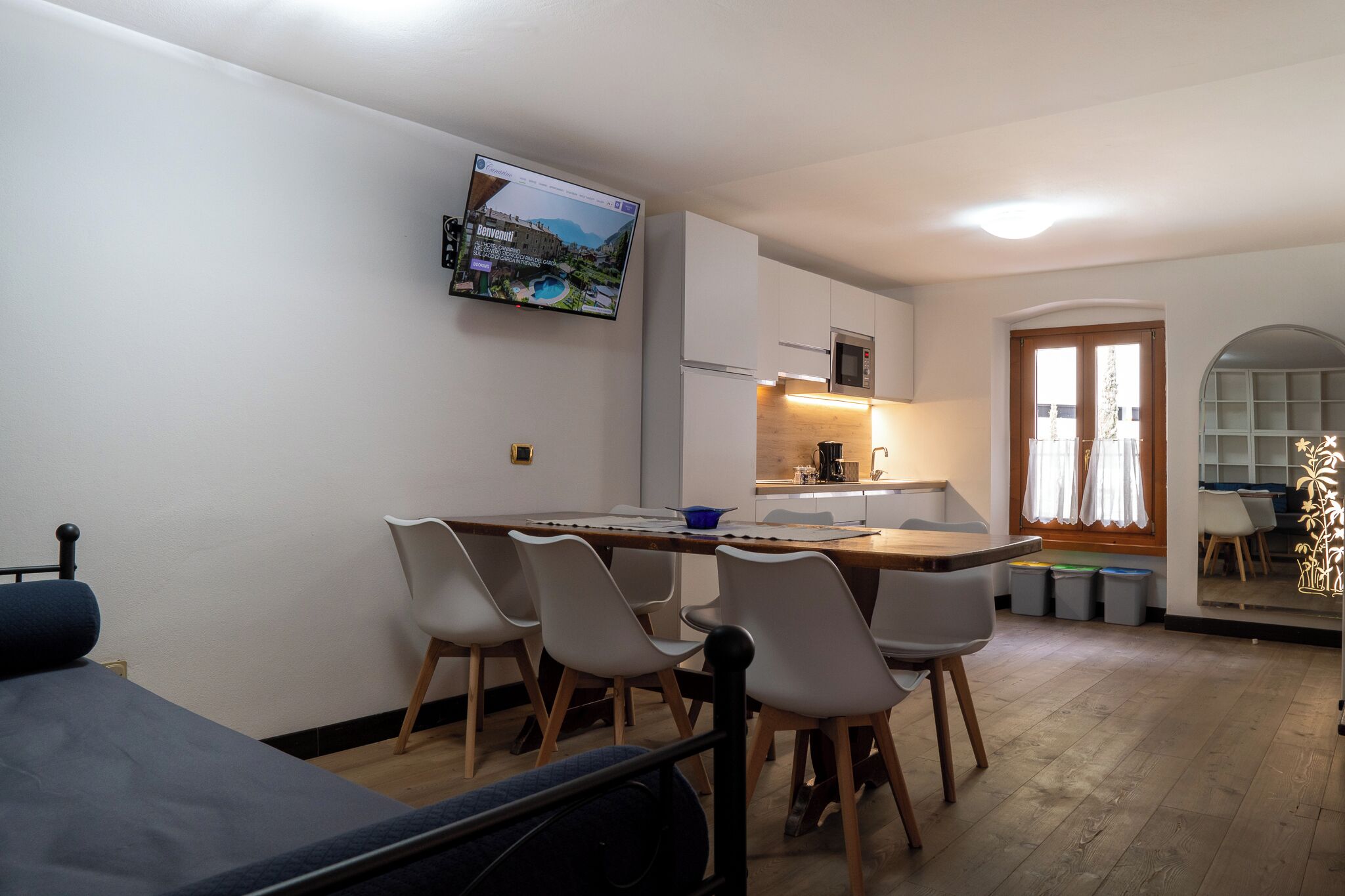 Un espace de vie compact comprenant un coin cuisine, un coin repas avec des chaises, un lit et un téléviseur fixé au mur qui diffuse une image panoramique.