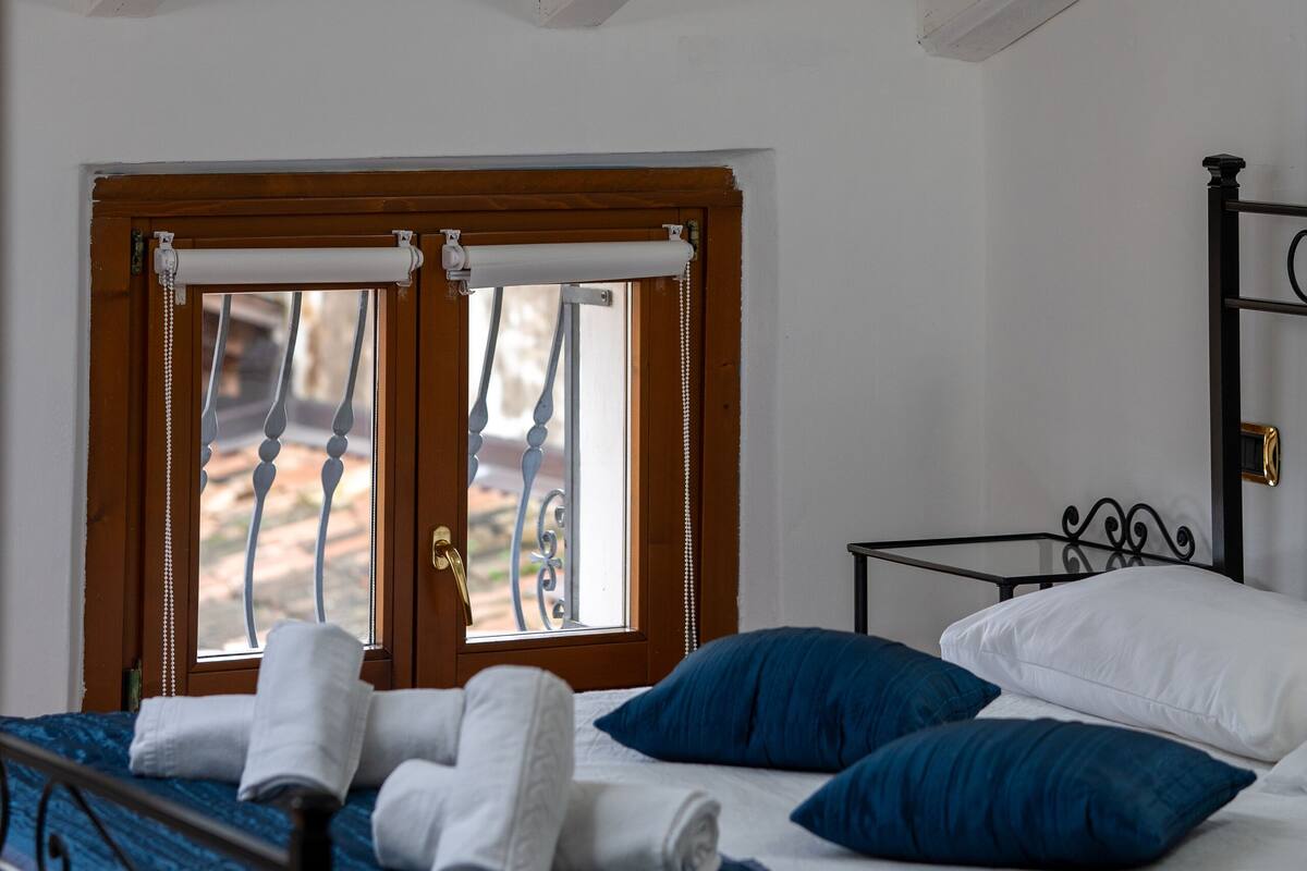 Een slaapkamer met een bed, kussens en een raam met gordijnen.