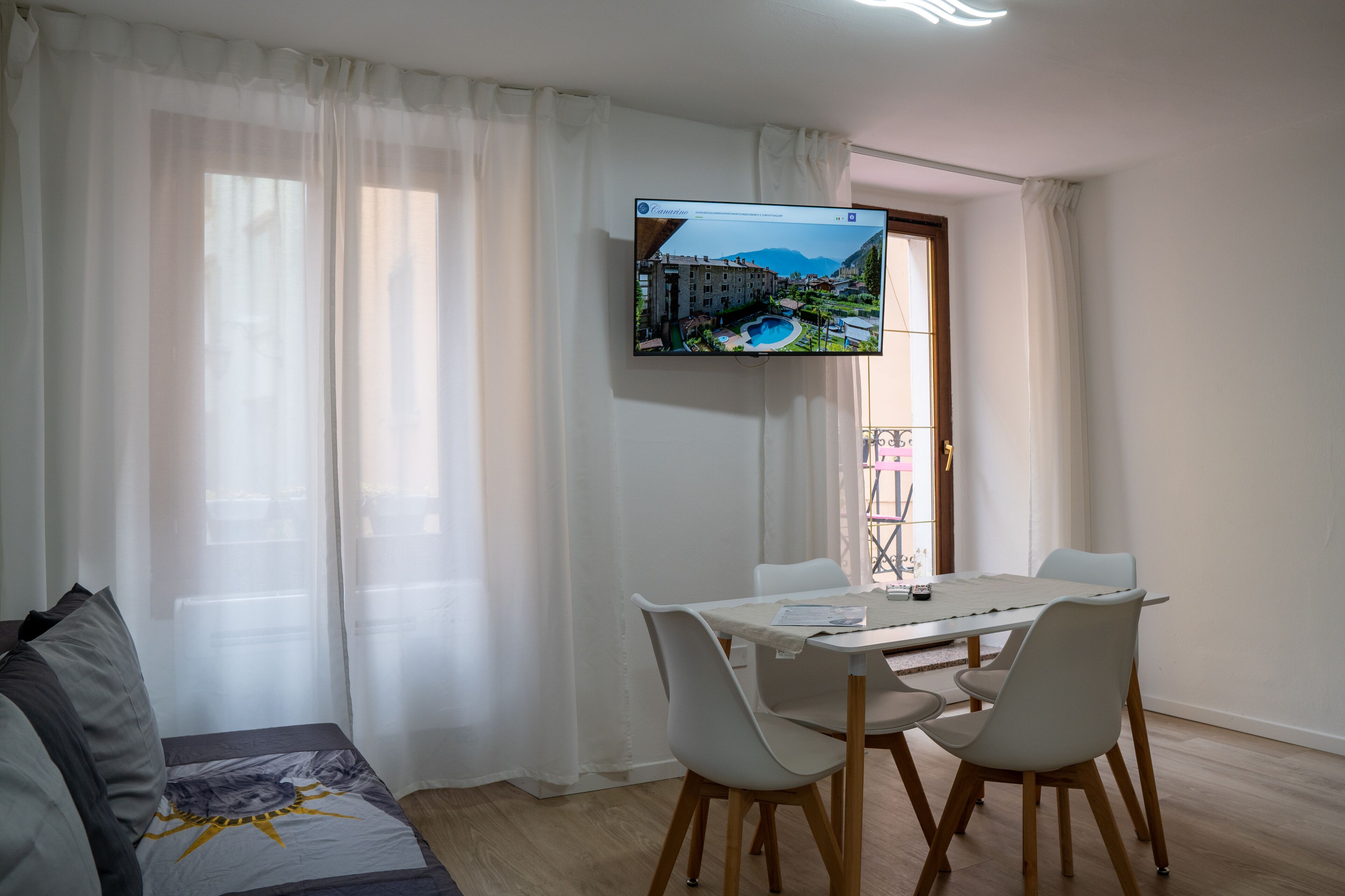 Ein modernes Wohnzimmer mit Essbereich, einem an der Wand montierten Flachbildfernseher und Blick auf ein Gebäude durch das Fenster.