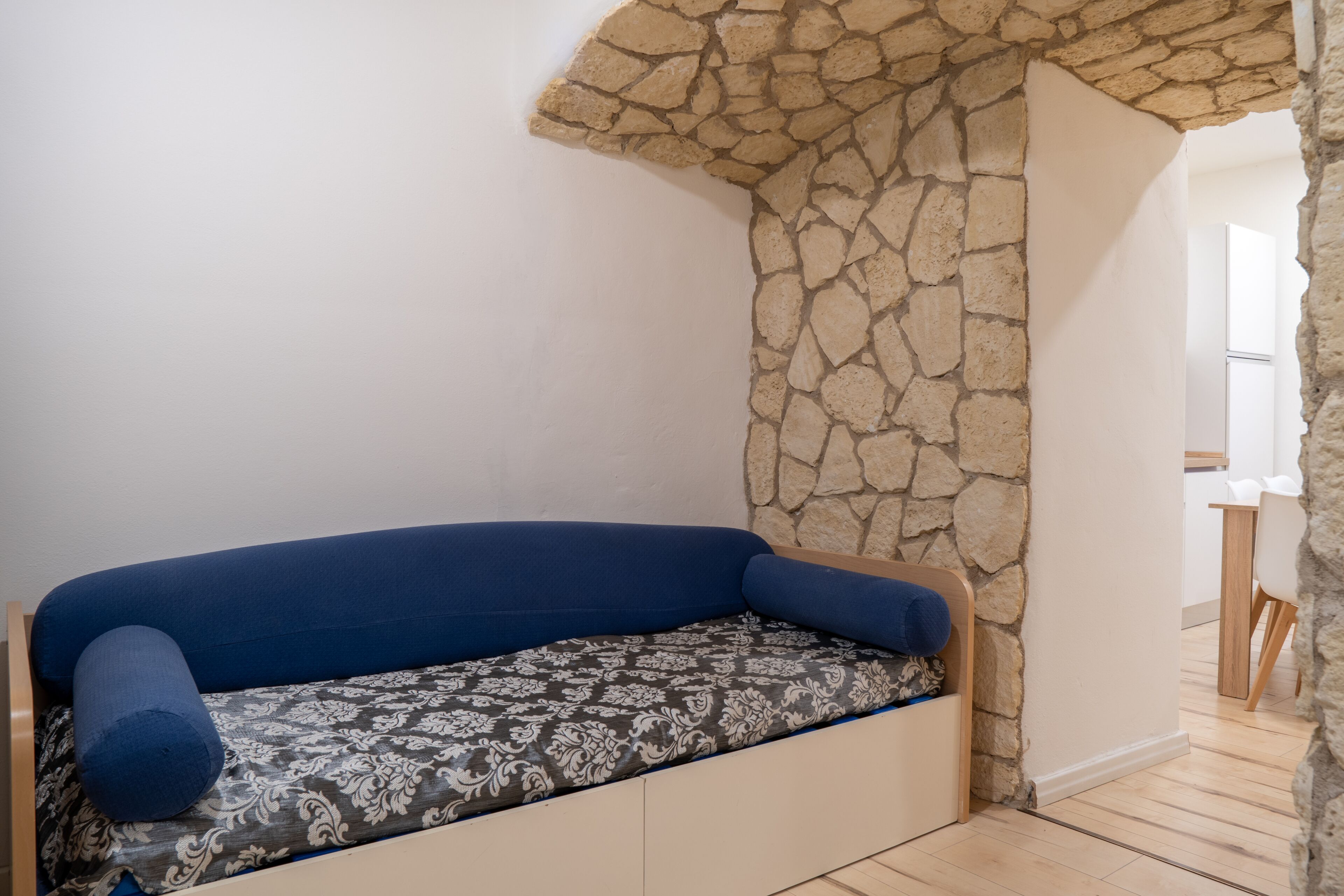 A small, cozy room with a stone wall, a blue cushioned bench, and a wooden table.