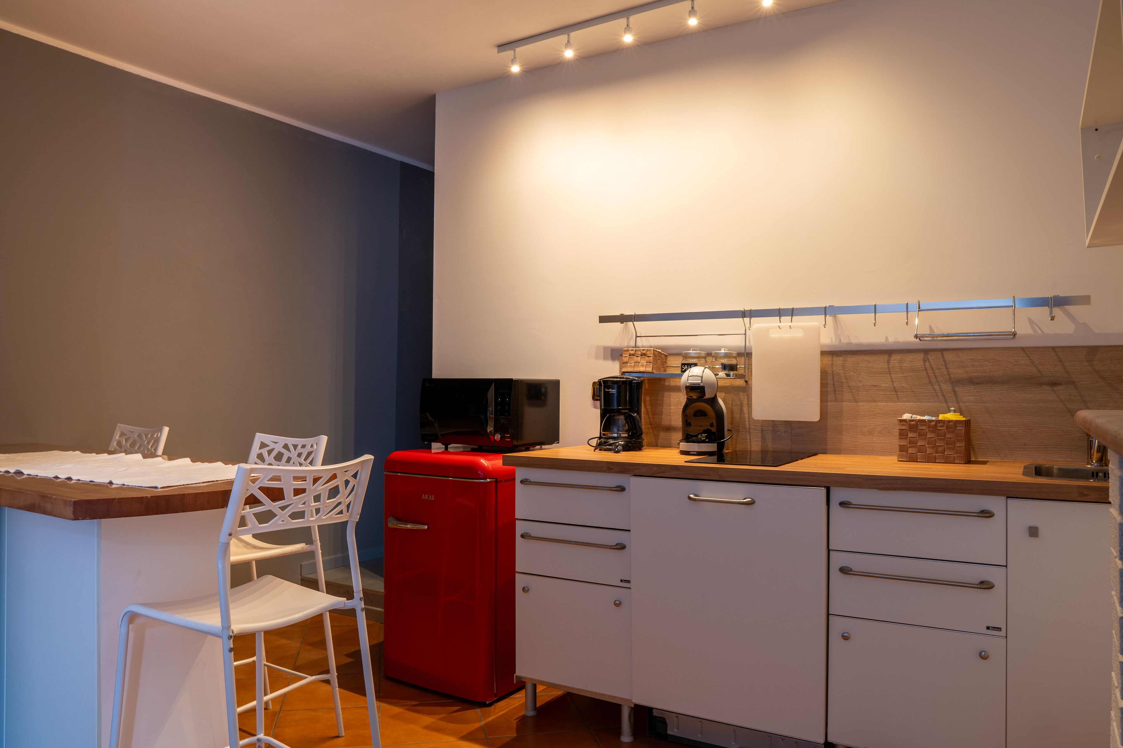 A compact kitchen with a dining area, featuring a red refrigerator, white cabinets, and a wooden countertop.