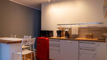 A compact kitchen with a dining area, featuring a red refrigerator, white cabinets, and a wooden countertop.
