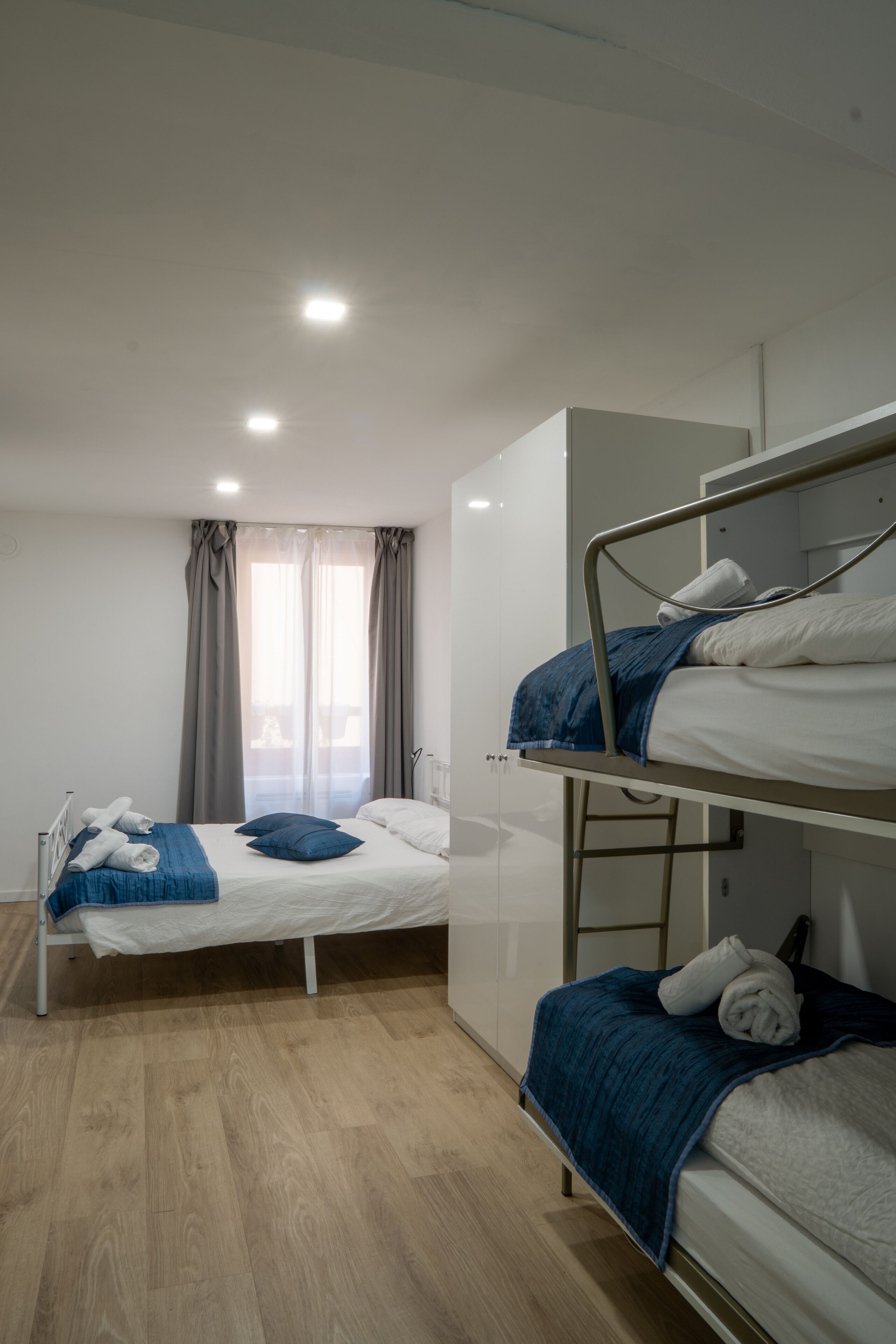 A dormitory room with bunk beds, a wardrobe, and a window with curtains.