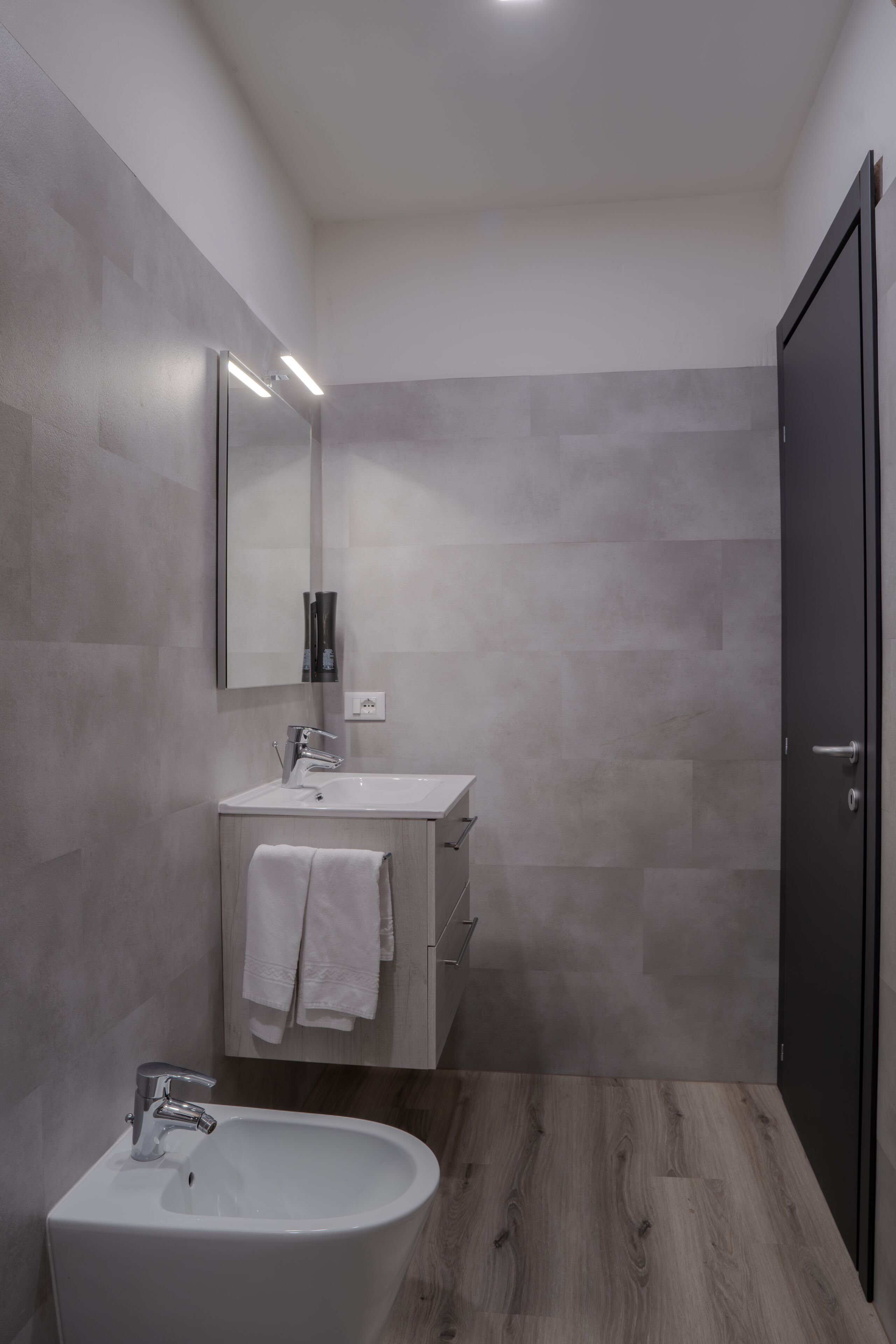 A modern bathroom with a white sink, mirror, and wooden flooring.
