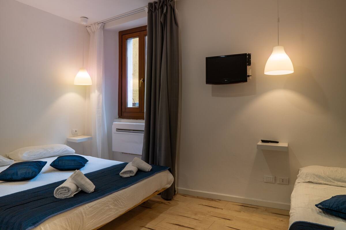 Een hotelkamer met een bed, een aan de muur bevestigde televisie en een raam met gordijnen.