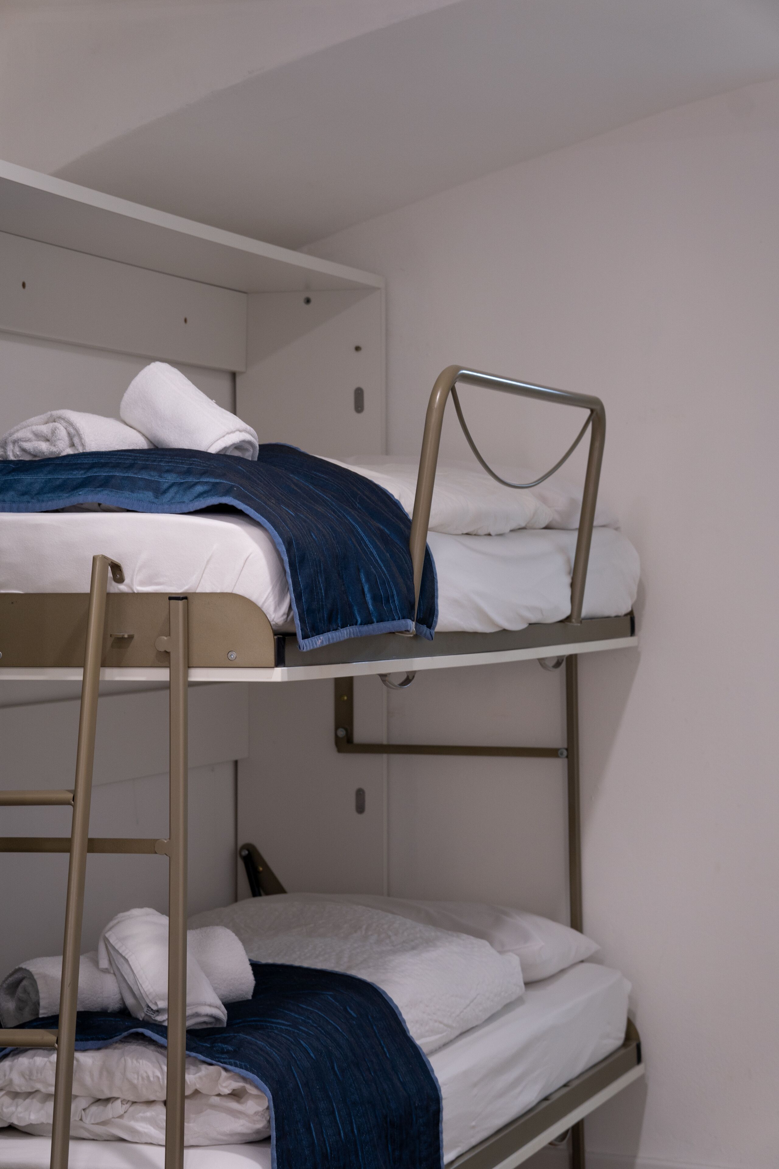 Una cama litera con ropa de cama blanca y una manta azul.