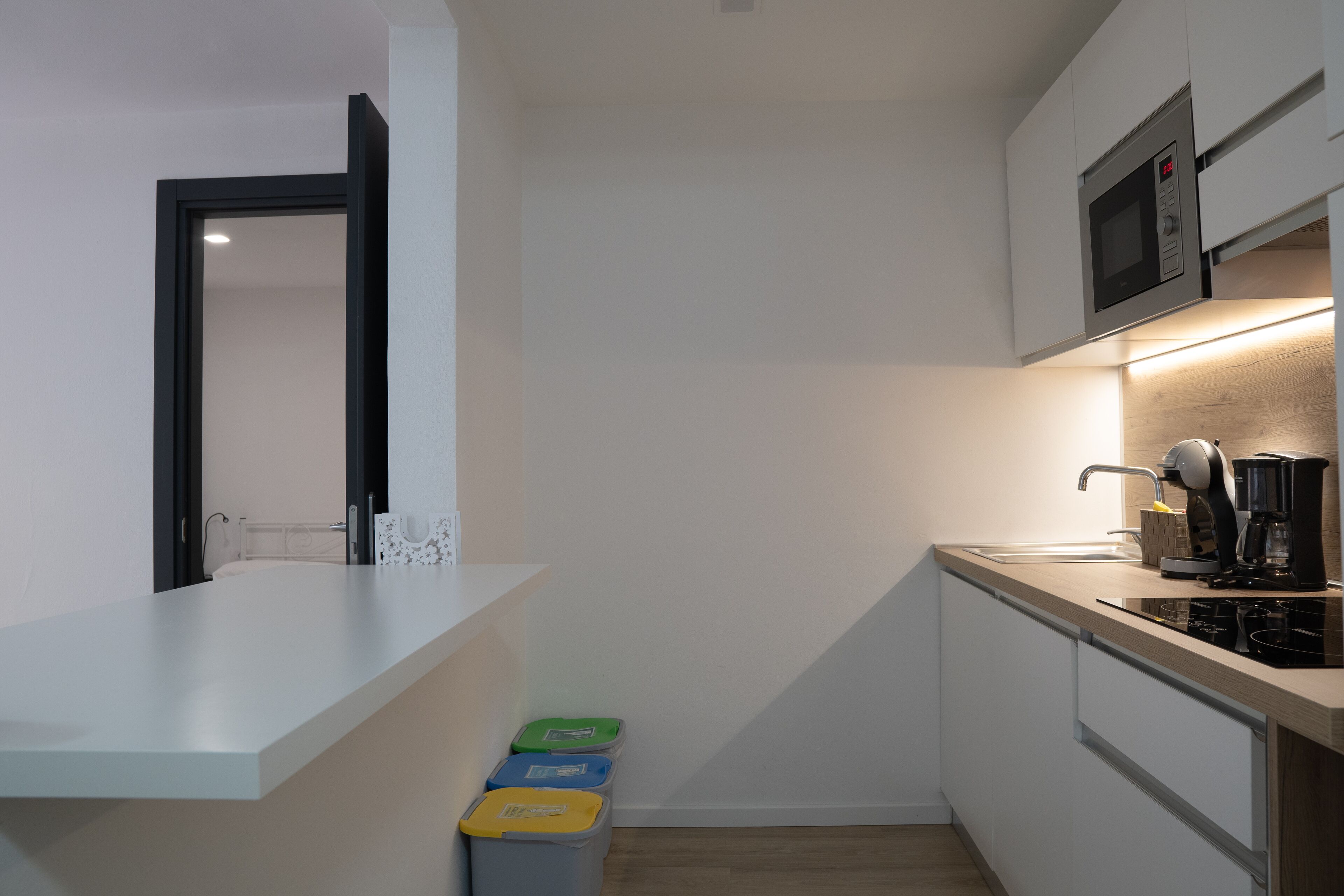 A compact kitchen with a microwave, coffee maker, and trash bins.