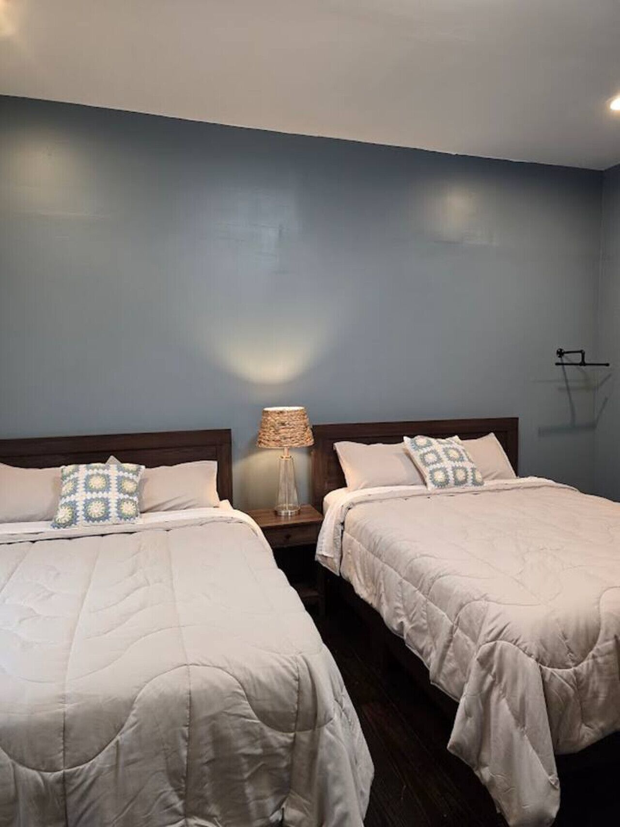 A hotel room with two beds, a nightstand with a lamp, and a wall-mounted light fixture.