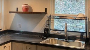 Eine Küche mit Spüle aus Edelstahl, einem Fenster mit Blick auf Grünflächen und einer Popcorndose auf einem Regal.