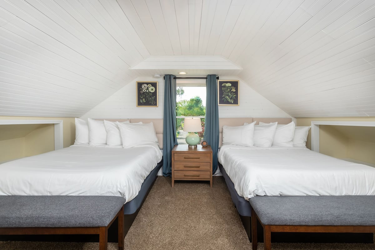 A bedroom with two beds, a nightstand, and a view of the outdoors.