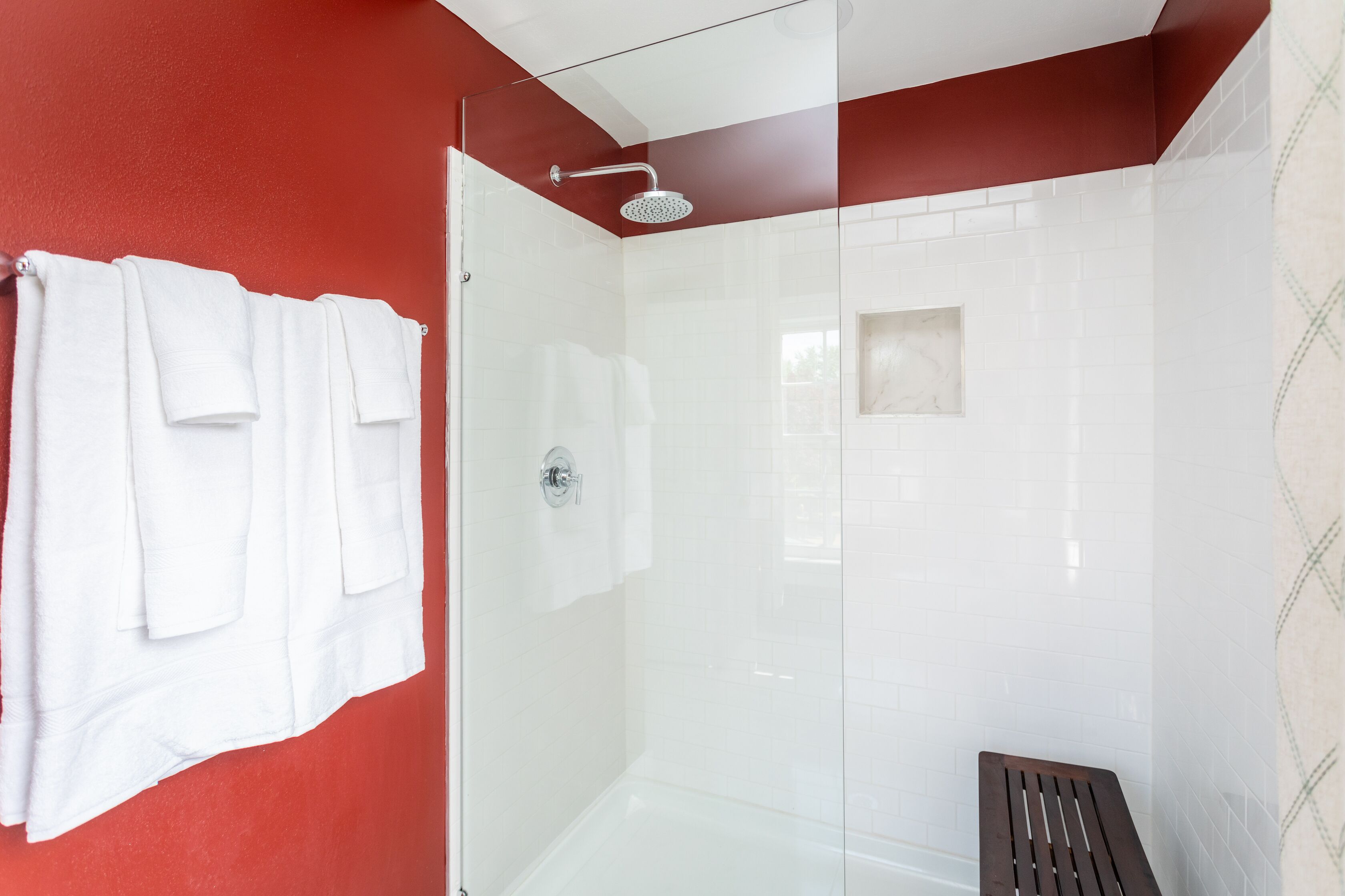 A modern bathroom with a glass shower enclosure, white tiled walls, and a red accent wall.