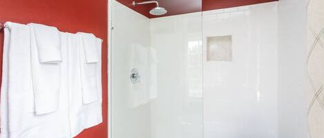 Ein modernes Badezimmer mit Duschkabine aus Glas, weißen Fliesenwänden und einer roten Akzentwand.