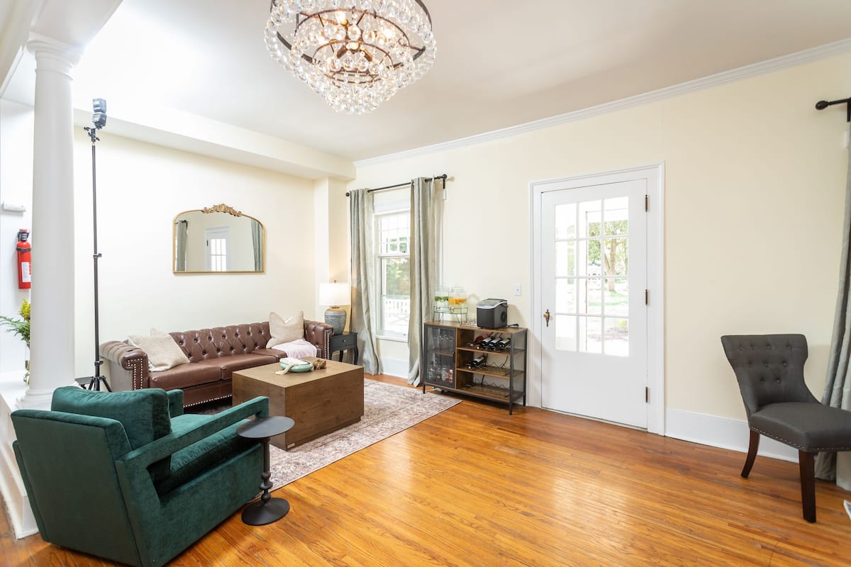 A spacious living room with a brown leather sofa, a green armchair, a wooden coffee table, and a chandelier.