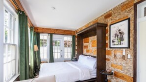 A bedroom with a bed, green curtains, a wooden headboard, a framed picture, and a corkboard wall. - The Legacy Inn (Luray)