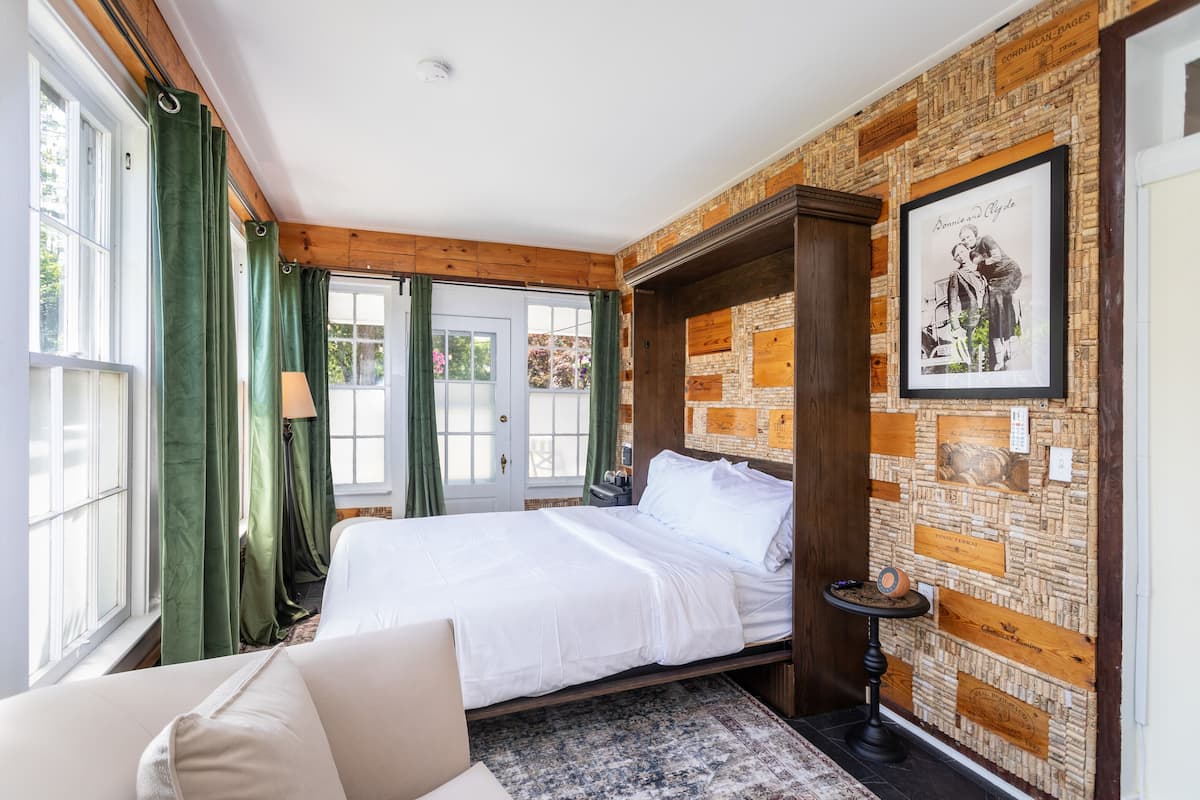 A bedroom with a bed, green curtains, a wooden headboard, a framed picture, and a corkboard wall.