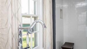 A bathroom with a modern faucet, a window with curtains, and a small wooden bench. - The Legacy Inn (Luray)