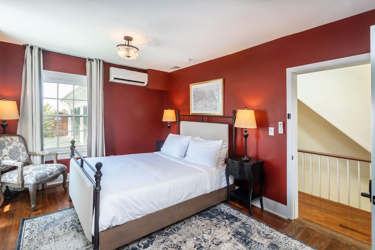 A bedroom with a large bed, two bedside lamps, a chair, and a window with curtains.