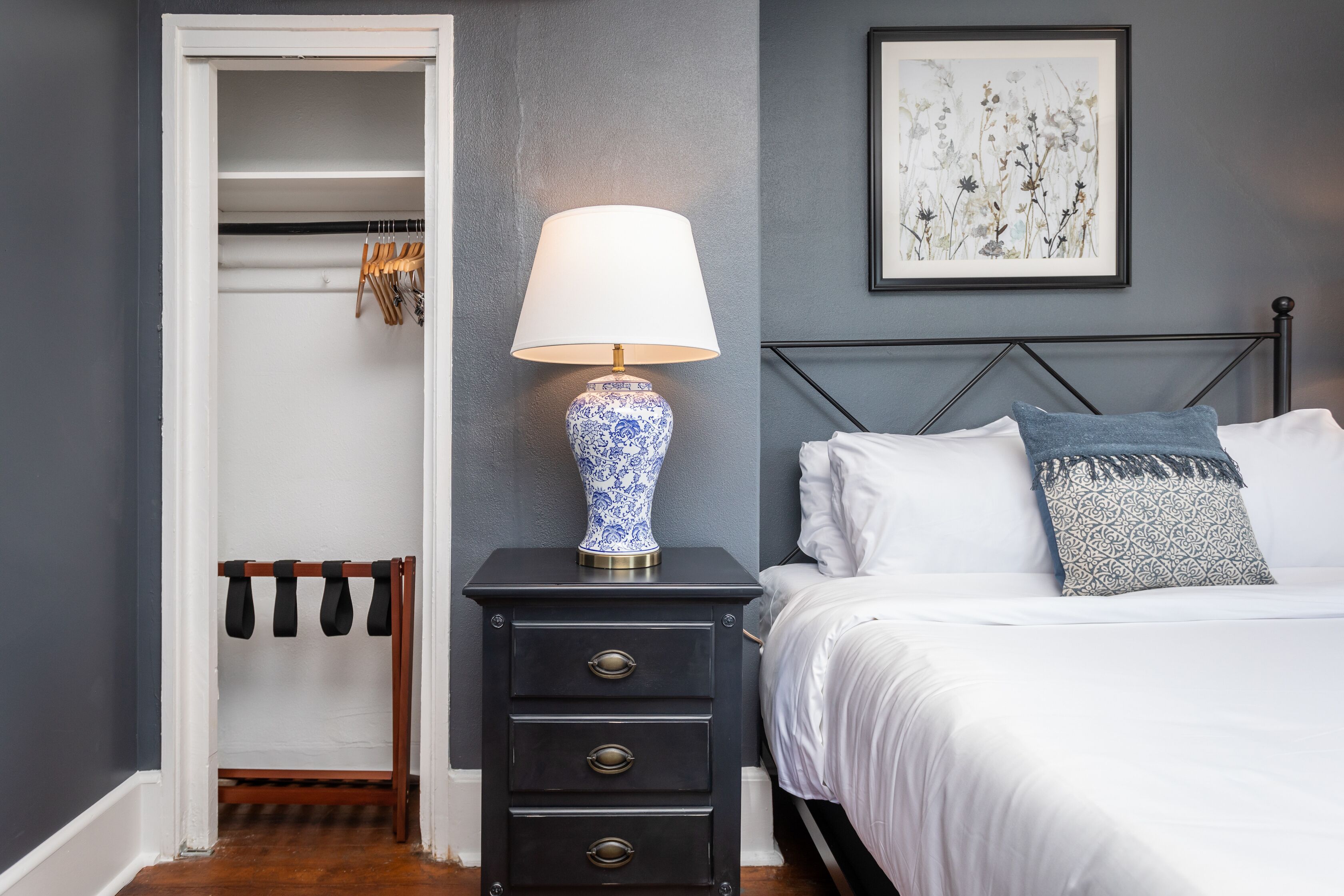 A bedroom with a bed, a nightstand with a lamp, a wardrobe, and a framed artwork on the wall.