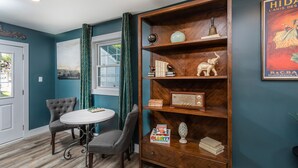 A room with teal walls, a wooden bookshelf, a round table with two chairs, and a window with curtains. - The Legacy Inn (Luray)