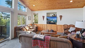 A cozy living room with a wooden ceiling, large windows, a sofa, a coffee table, and a fireplace. - Whispering Pines in Tahoe Vista (Tahoe Vista)