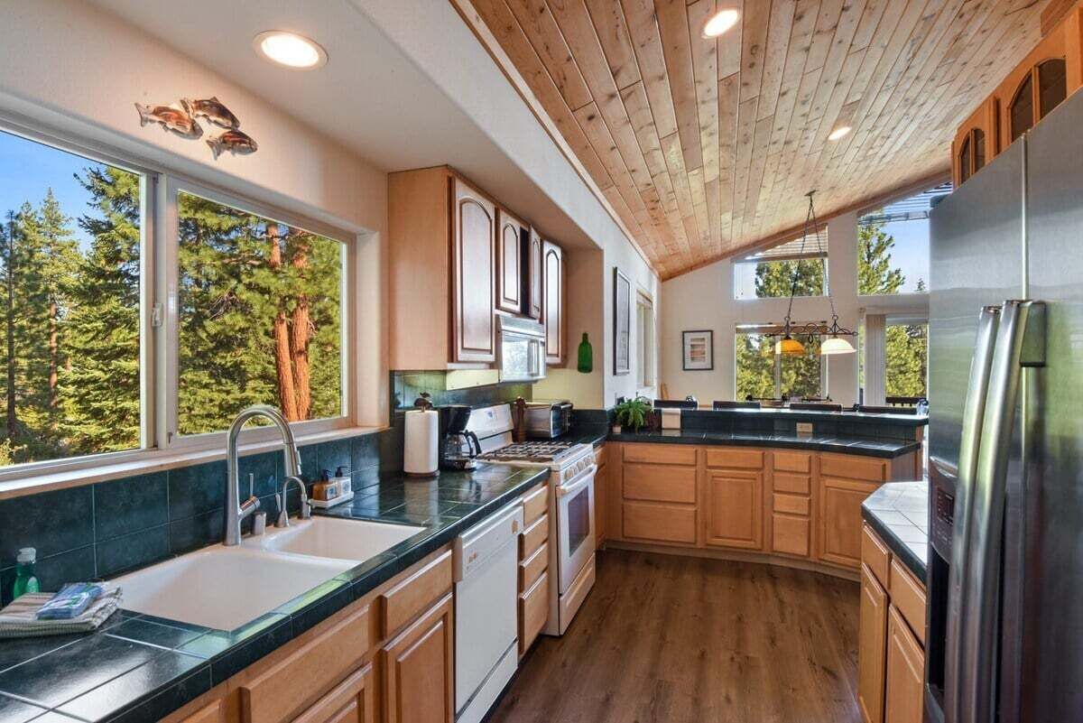 Une cuisine moderne avec des meubles en bois, un réfrigérateur en acier inoxydable et une grande fenêtre donnant sur la verdure.