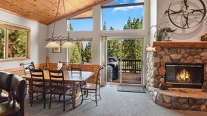 A cozy interior with a stone fireplace, wooden ceiling, and large windows offering a view of the outdoors. - Whispering Pines in Tahoe Vista (Tahoe Vista)