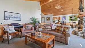 A cozy living room with a fireplace, wooden ceiling, and a dining area in the background. - Whispering Pines in Tahoe Vista (Tahoe Vista)